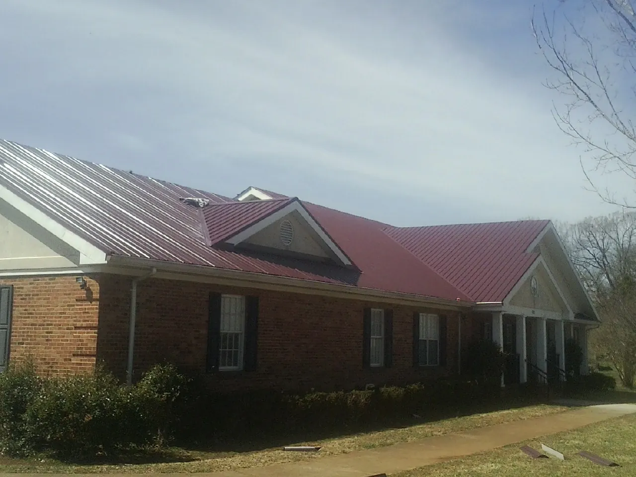 Red metal roof with gabled entries on a long brick building, from a Hail Damage Roof Repair job in Pleasant Hill