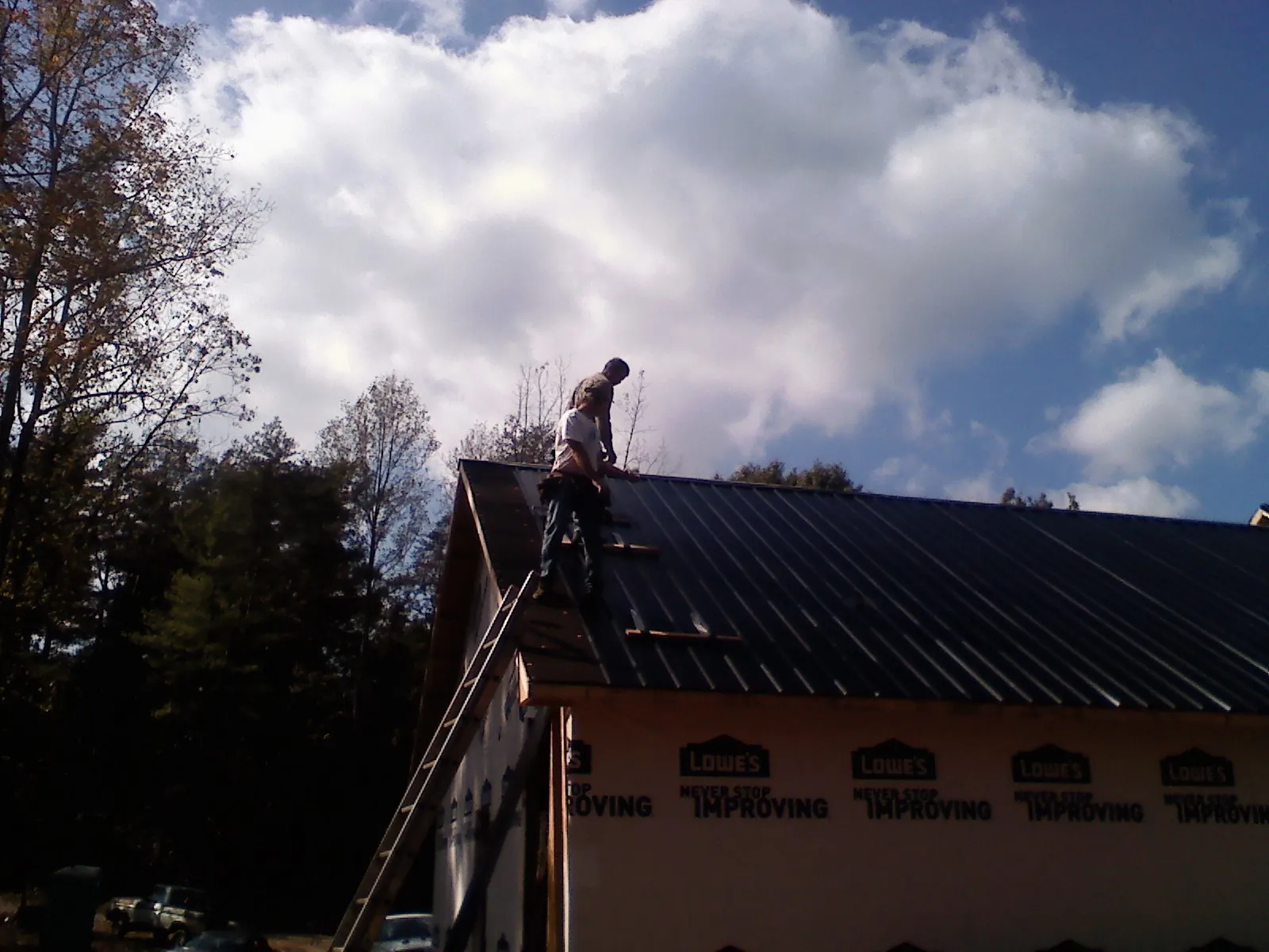 Roofer fastening dark metal panels high against a cloudy sky, from a Roof Inspection job in Pleasant Hill